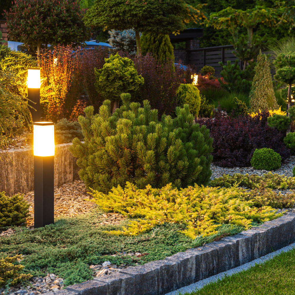 Moderne tuinverlichting LED sokkellamp in een sfeervol aangelegde tuin bij schemering, zijaanzicht met meerdere verlichte lampen langs een verhoogd plantenbed.