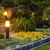 Moderne tuinverlichting LED sokkellamp in een sfeervol aangelegde tuin bij schemering, zijaanzicht met meerdere verlichte lampen langs een verhoogd plantenbed.