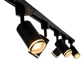 Zwarte moderne railverlichting met kantelbare cilindervormige spots, diagonaal van onderaf gefotografeerd, met warme LED-verlichting in elk van de vier spots.