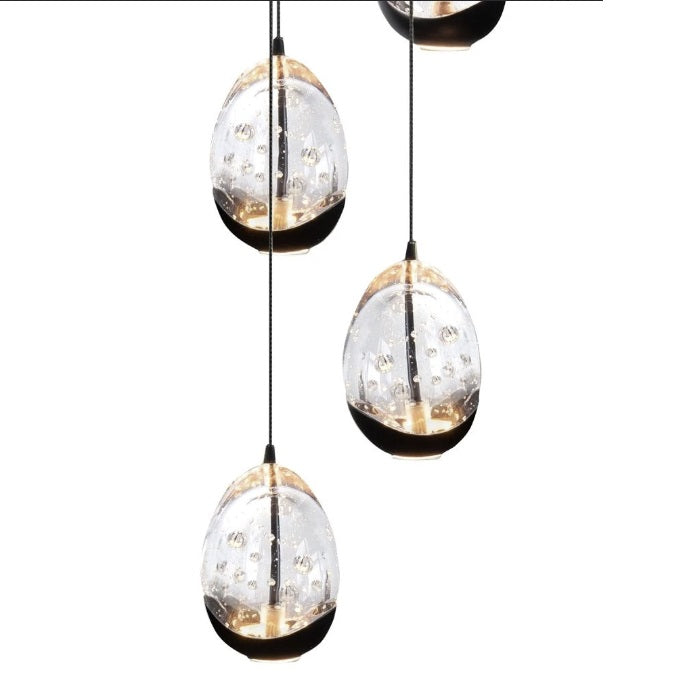 Close-up vooraanzicht van moderne hanglampen in druppelvorm met glazen behuizing en geïntegreerde LED-verlichting, hangend aan zwarte snoeren tegen een witte achtergrond.