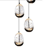 Close-up vooraanzicht van moderne hanglampen in druppelvorm met glazen behuizing en geïntegreerde LED-verlichting, hangend aan zwarte snoeren tegen een witte achtergrond.