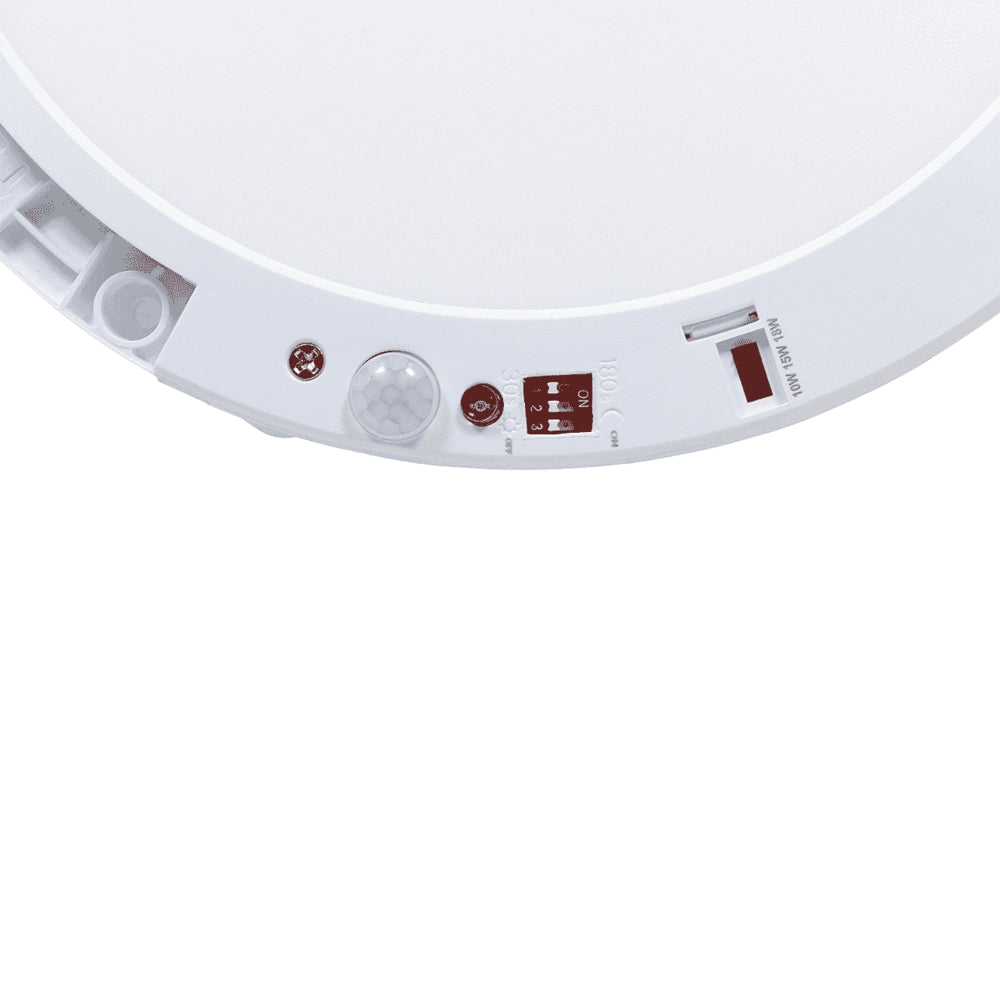 Detailaanzicht van de onderzijde van een witte LED plafondlamp met geïntegreerde bewegingssensor en instelbare schuifschakelaars voor detectiebereik en lichtinstellingen.