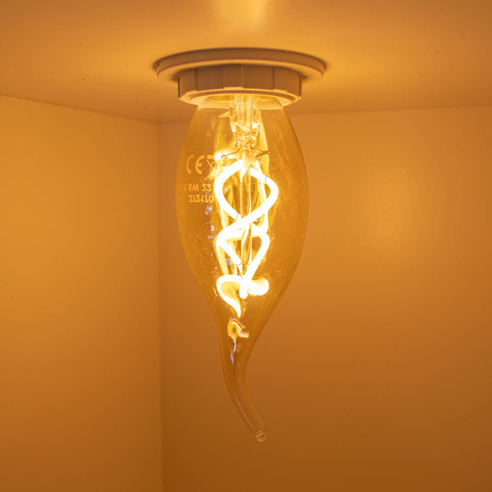 Close-up van een brandende decoratieve LED filamentlamp met spiraalvormig patroon, gemonteerd aan het plafond, gezien vanaf de zijkant met warme sfeerverlichting.