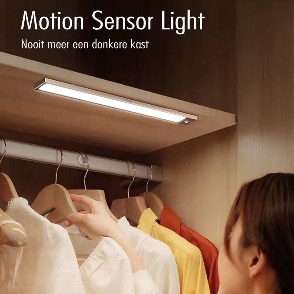 LED Motion Sensor Light gemonteerd aan het plafond van een houten kledingkast, verlicht kledij op hangers terwijl een persoon kleding uitkiest – ideaal voor donkere kasten zonder verlichting, vooraanzicht binnenin de kast.