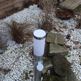 RVS buitenlamp met stopcontact, cilindervormig model, staand afgebeeld in een tuin met grind en sierstenen – bovenaanzicht.