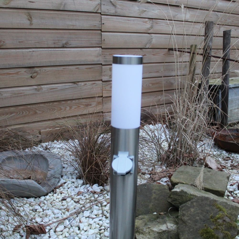 RVS buitenlamp met stopcontact in moderne tuin, frontaal aanzicht tegen houten schutting en siergrind.