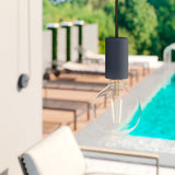 Moderne hanglamp met zwarte fitting en ronde LED gloeilamp, close-up aanzicht, gemonteerd boven een luxe buitenzwembad met ligstoelen op de achtergrond.